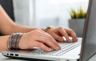 image of a lady typing on a laptop a blog post about five reasons to hire a marketing firm