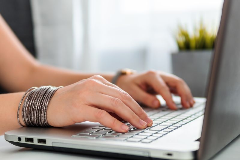 image of a lady typing on a laptop a blog post about five reasons to hire a marketing firm
