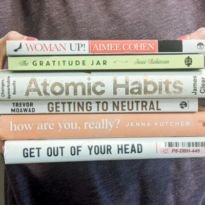 Kayla holding a stack of books reading The gratitude jar, Atomic Habits, Getting to Neutral, How are you, really?, Get out of your head